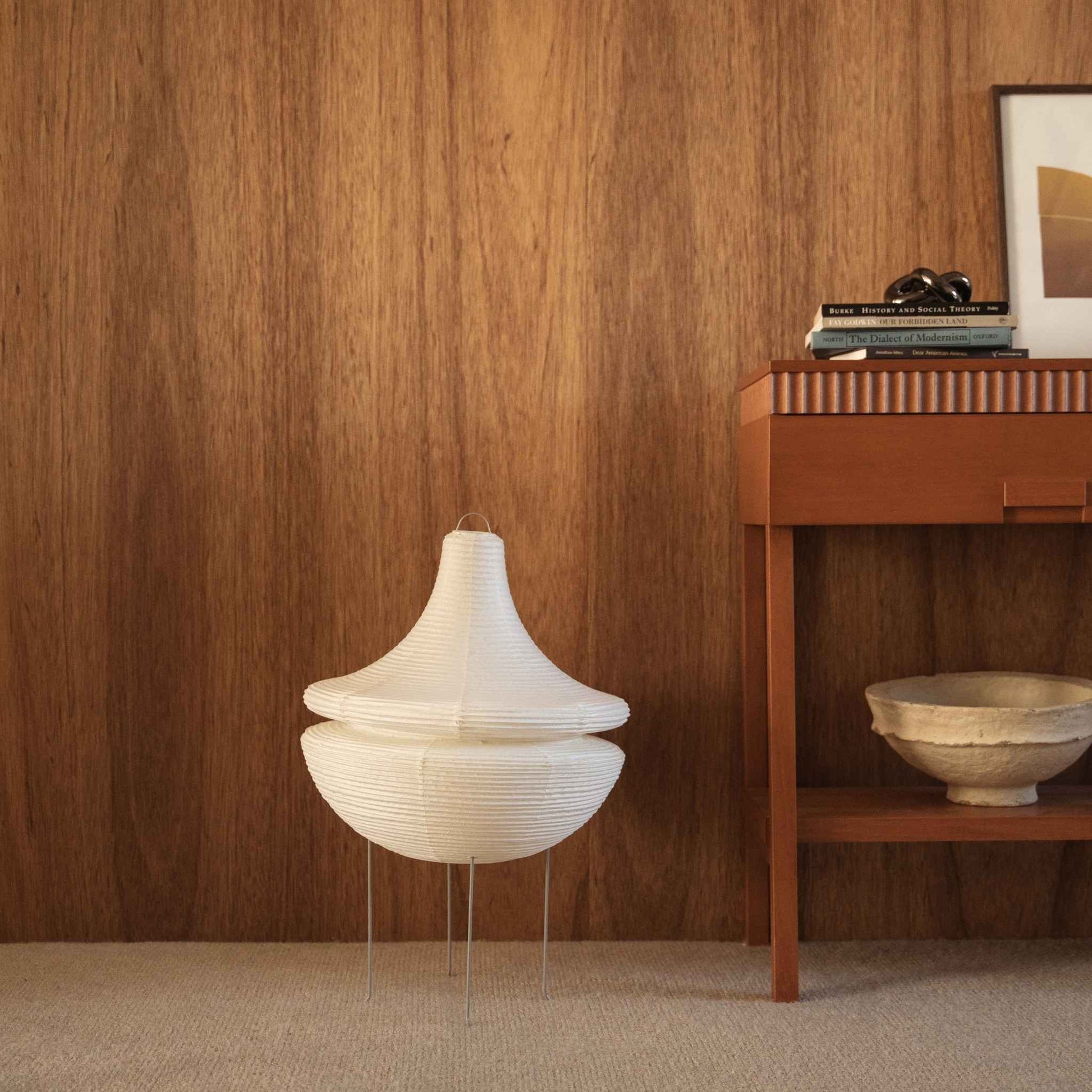 Lampe sur pied japonaise non allumée en papier Gemini 02 posée sur un tapis à côté d'une console en bois devant un mur sombre