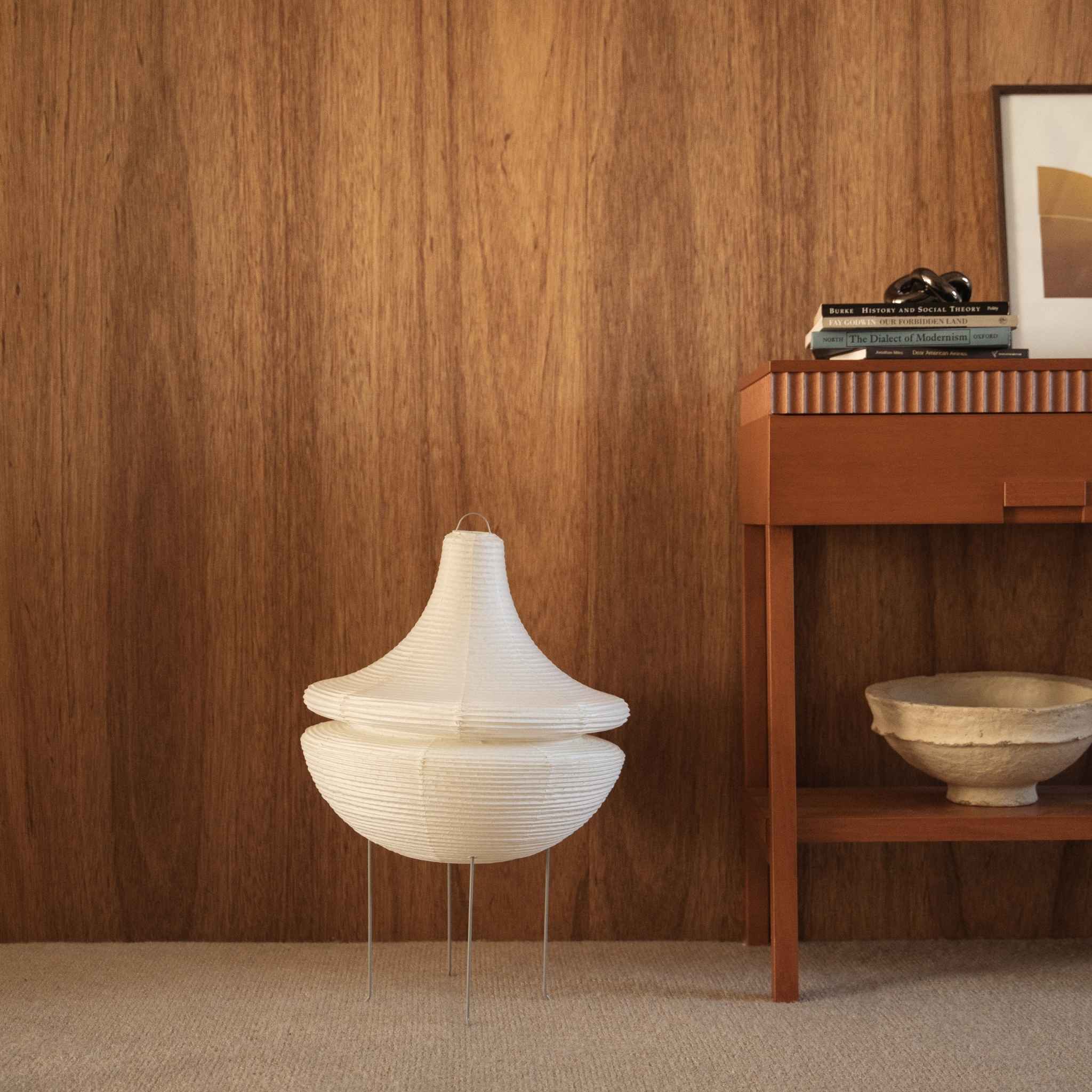 Lampe sur pied japonaise non allumée en papier Gemini 02 posée sur un tapis à côté d'une console en bois devant un mur sombre
