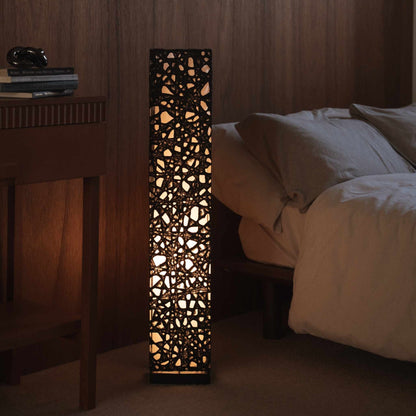"Lampe sur pied en papier japonais noir Me Look 01, placée à côté d'un lit dans une chambre japonaise faiblement éclairée."