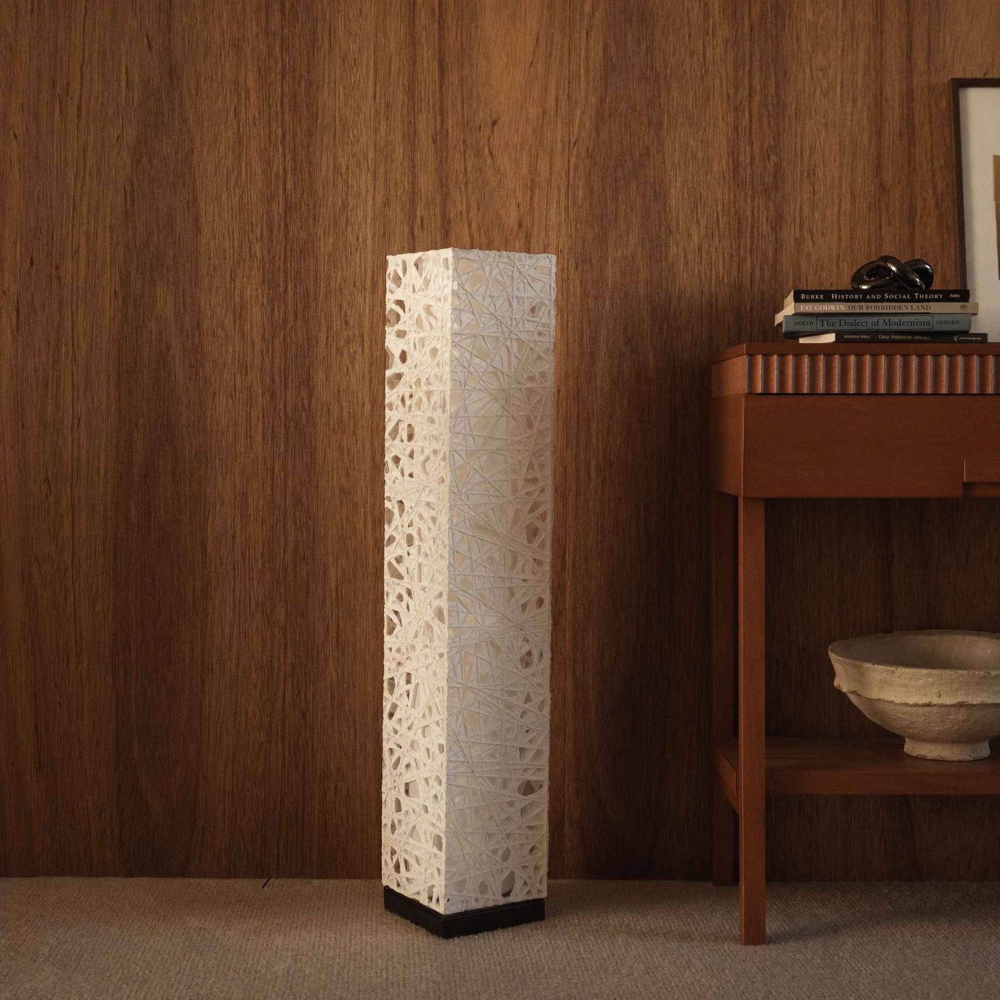"Lampe japonaise Me Look 01 blanche et haute en papier, debout, non allumée, à côté d'une console en bois dans un salon."