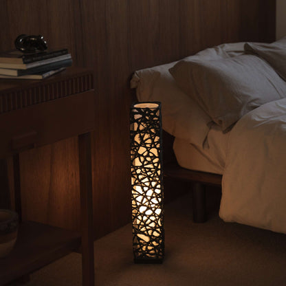 "Lampe sur pied en papier japonais noir Me Look 02, éclairant chaleureusement à côté d'un lit dans une chambre japonaise."