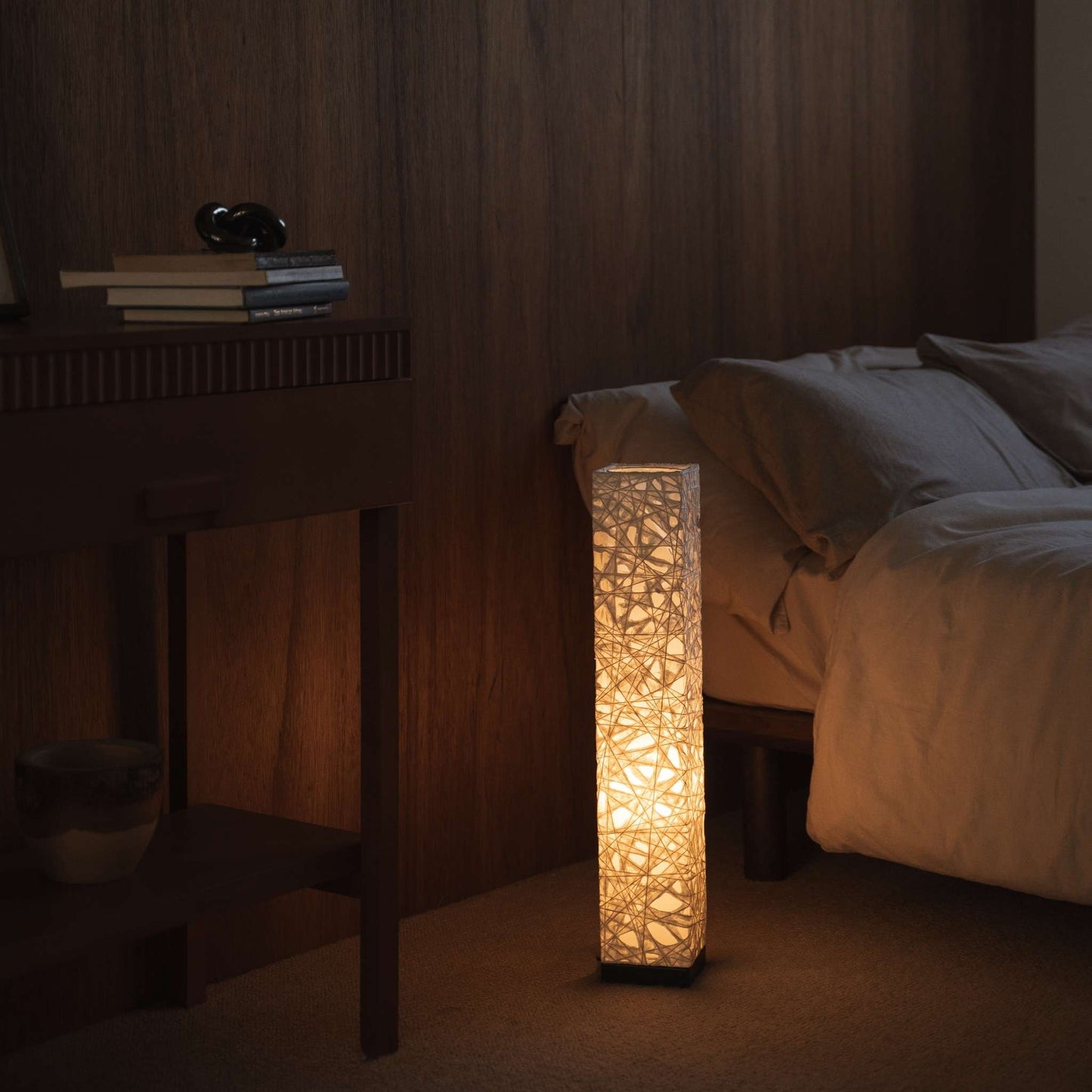 "Lampe sur pied en papier japonais blanc Me Look 02, éclairant chaleureusement à côté d'un lit dans une chambre japonaise."