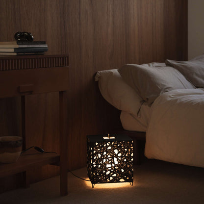 "Lampe japonaise en papier Me-Look 03 en forme de cube, noire, diffusant une lumière chaude sur une table de chevet en bois dans une chambre japonaise."
