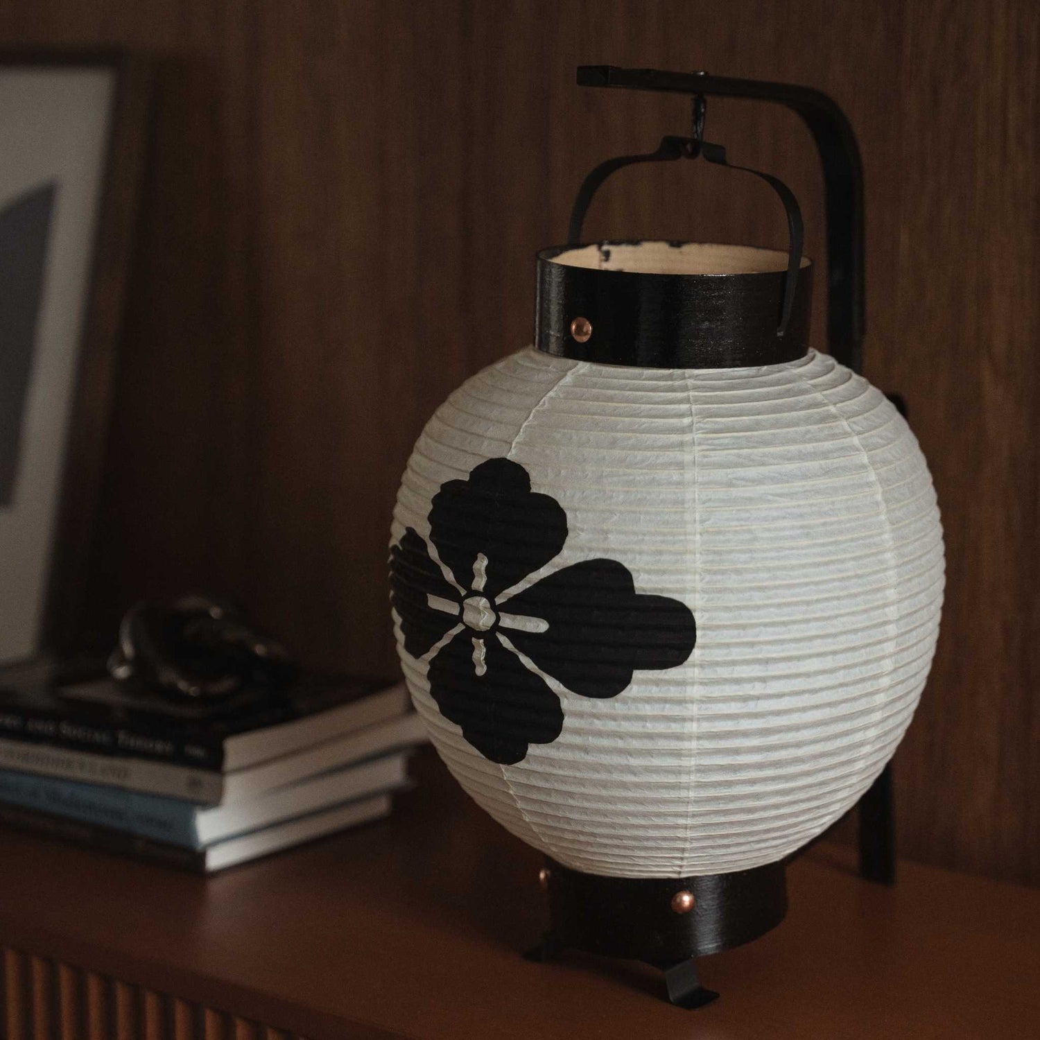 Close-up van een onverlichte Japanse chochin-lantaarn die de handgemaakte washi-papieren textuur en een bloemmotief in zwarte inkt toont.