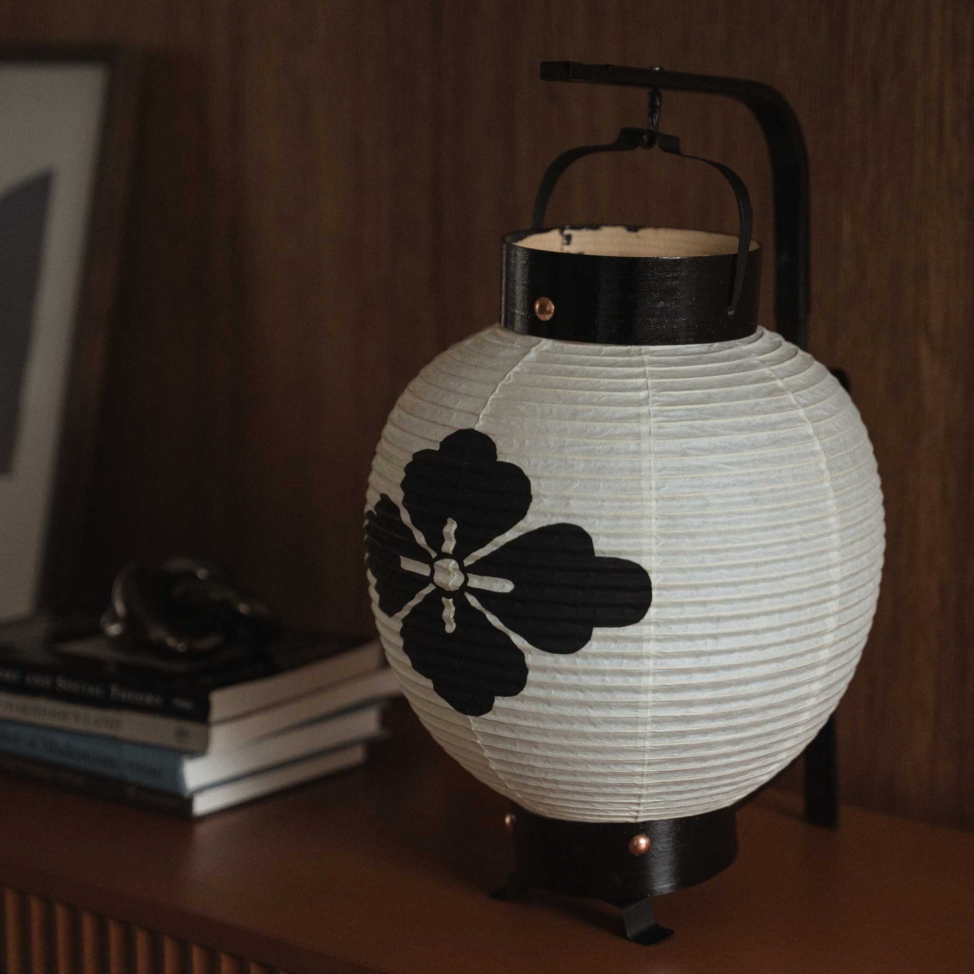 Close-up van een onverlichte Japanse chochin-lantaarn die de handgemaakte washi-papieren textuur en een bloemmotief in zwarte inkt toont.