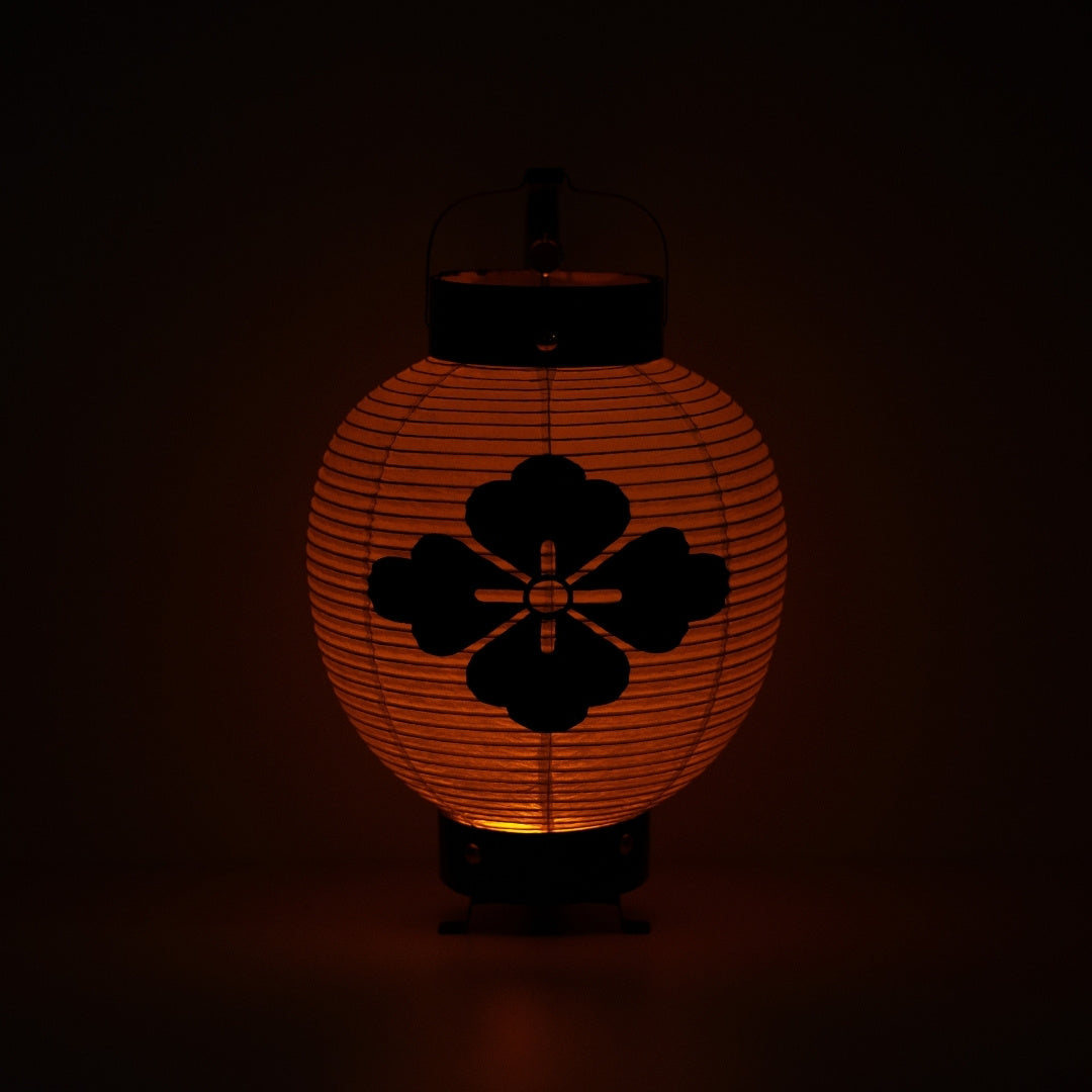 Een Japanse lantaarn met bloemdiamant verlicht in het donker, die een meditatief oranje licht door het papieren lichaam werpt.