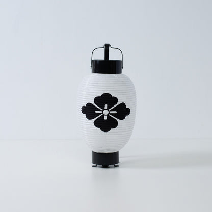 "Een witte Japanse papieren lantaarn met een handgeschilderd zwart bloemvormig hanabishi-embleem op een witte achtergrond."
