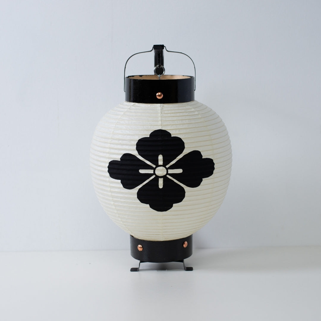 Een kleine Japanse papieren lantaarn met een handgeschilderd zwart bloemdiamant-embleem op wit washipapier.