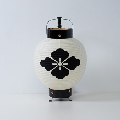 Een kleine Japanse papieren lantaarn met een handgeschilderd zwart bloemdiamant-embleem op wit washipapier.