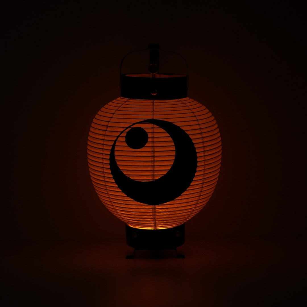 "Een Japanse papieren lantaarn die een warme oranje gloed verlicht in een donkere kamer, met de nadruk op het maan- en sterreninktschilderij."