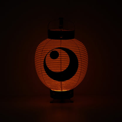 "Een Japanse papieren lantaarn die een warme oranje gloed verlicht in een donkere kamer, met de nadruk op het maan- en sterreninktschilderij."