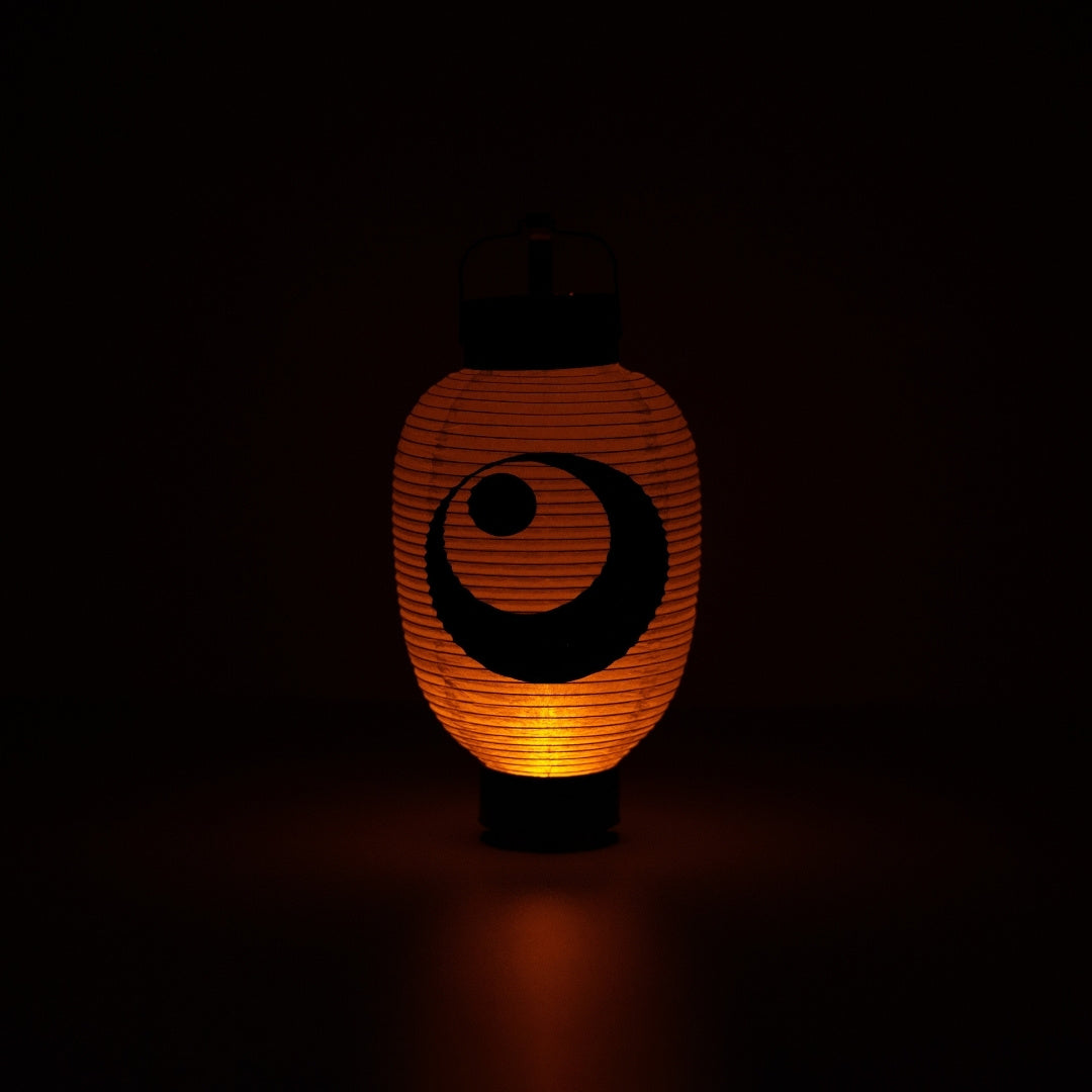 Verlichte Japanse papieren lantaarn met maan- en sterrenontwerp die een warme oranje gloed werpt in een donkere kamer.