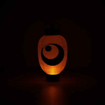 Verlichte Japanse papieren lantaarn met maan- en sterrenontwerp die een warme oranje gloed werpt in een donkere kamer.