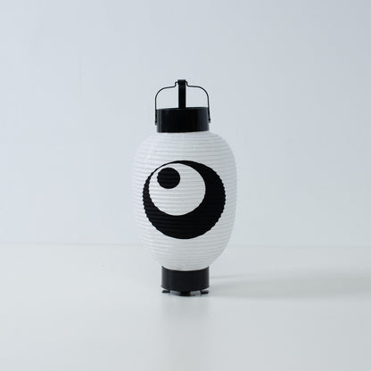 Een witte Japanse papieren lantaarn met een handgeschilderd zwart maan- en sterrenmotief, staand op een wit oppervlak.