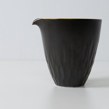 Carafe à saké en porcelaine noire avec motifs floraux sculptés - Gros plan sur une carafe à saké en porcelaine noire mate à la texture finement sculptée