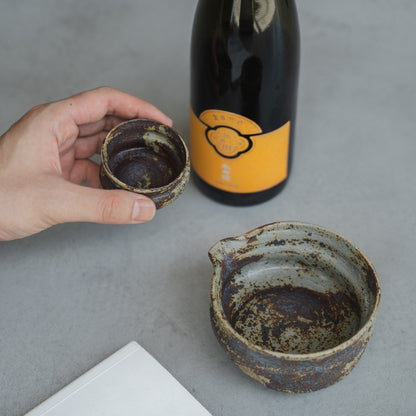 Japansk keramik sake-kop og karaffel på et moderne bord, holdt af en person, der nyder en fredelig tid med at læse alene.