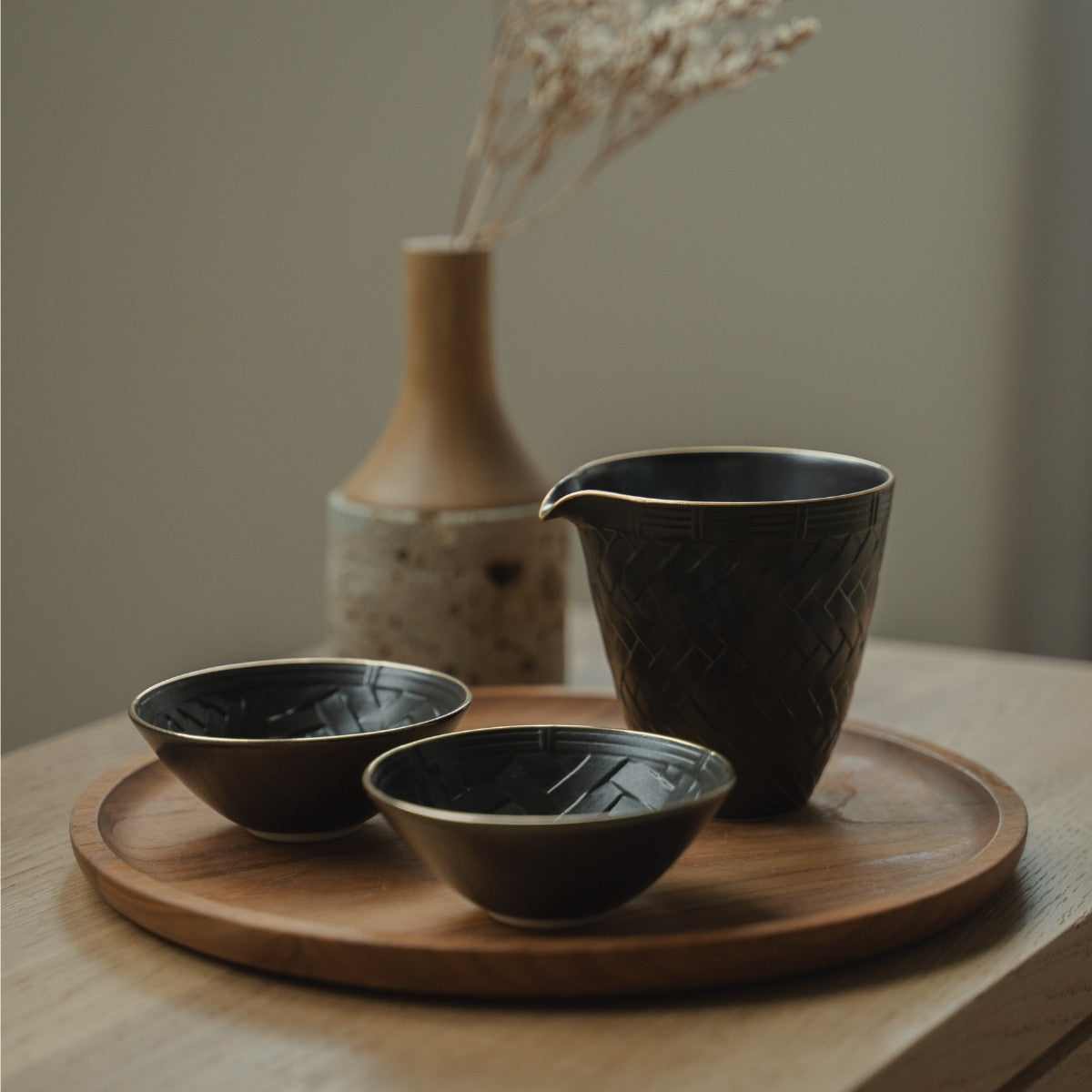 Schwarze Arita-Porzellan-Sake-Karaffe und Sake-Becher auf einem Holztablett, arrangiert für ein achtsames, modernes Esserlebnis.