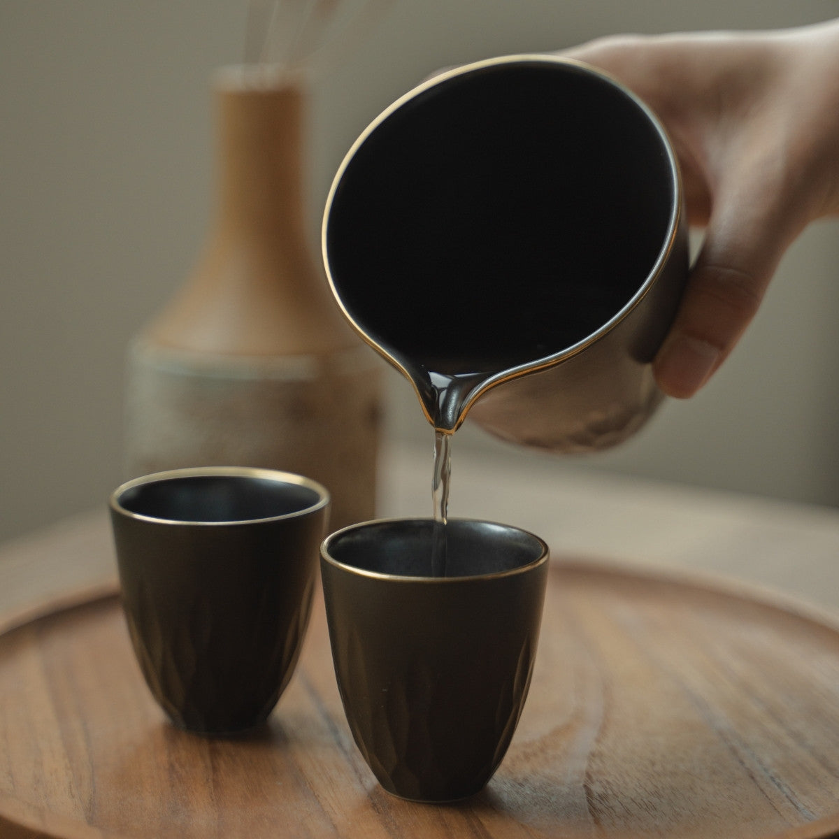 Verser à la main depuis un pichet à saké japonais noir mat dans une tasse assortie sur un plateau, rehaussant un dîner spécial.