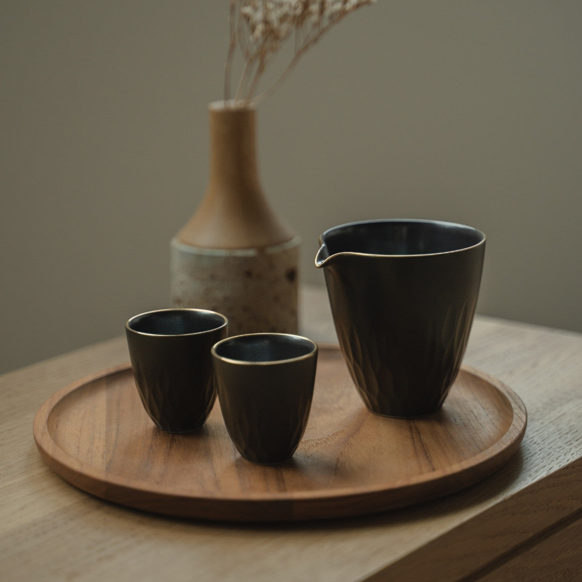 Carafe à saké en porcelaine arita noire et tasses guinomi sur un plateau en bois, invitant les amateurs de saké à une soirée raffinée.
