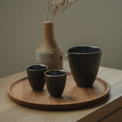 Carafe à saké en porcelaine arita noire et tasses guinomi sur un plateau en bois, invitant les amateurs de saké à une soirée raffinée.