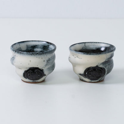 Two white and black Japanese sake cups ochoko Creative Cloud pottery from Japan, featuring an engraved black artisan seal on the front.