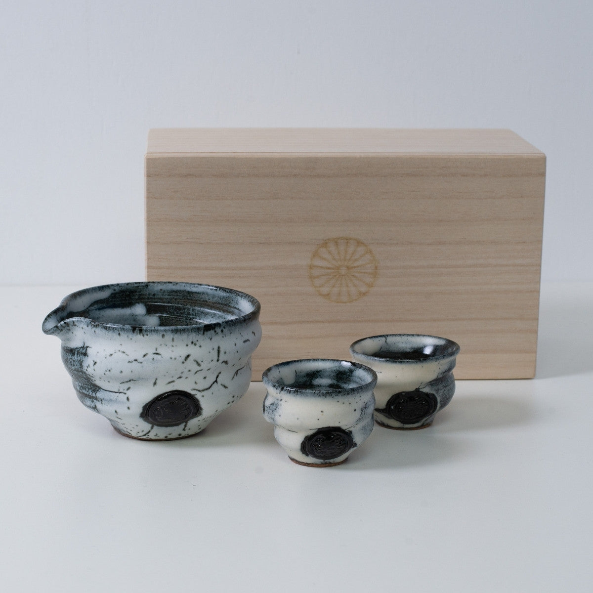 White and Black Japanese sake set "Creative Cloud" pottery with a sake carafe and two cups, next to a wooden box with a chrysanthemum crest.