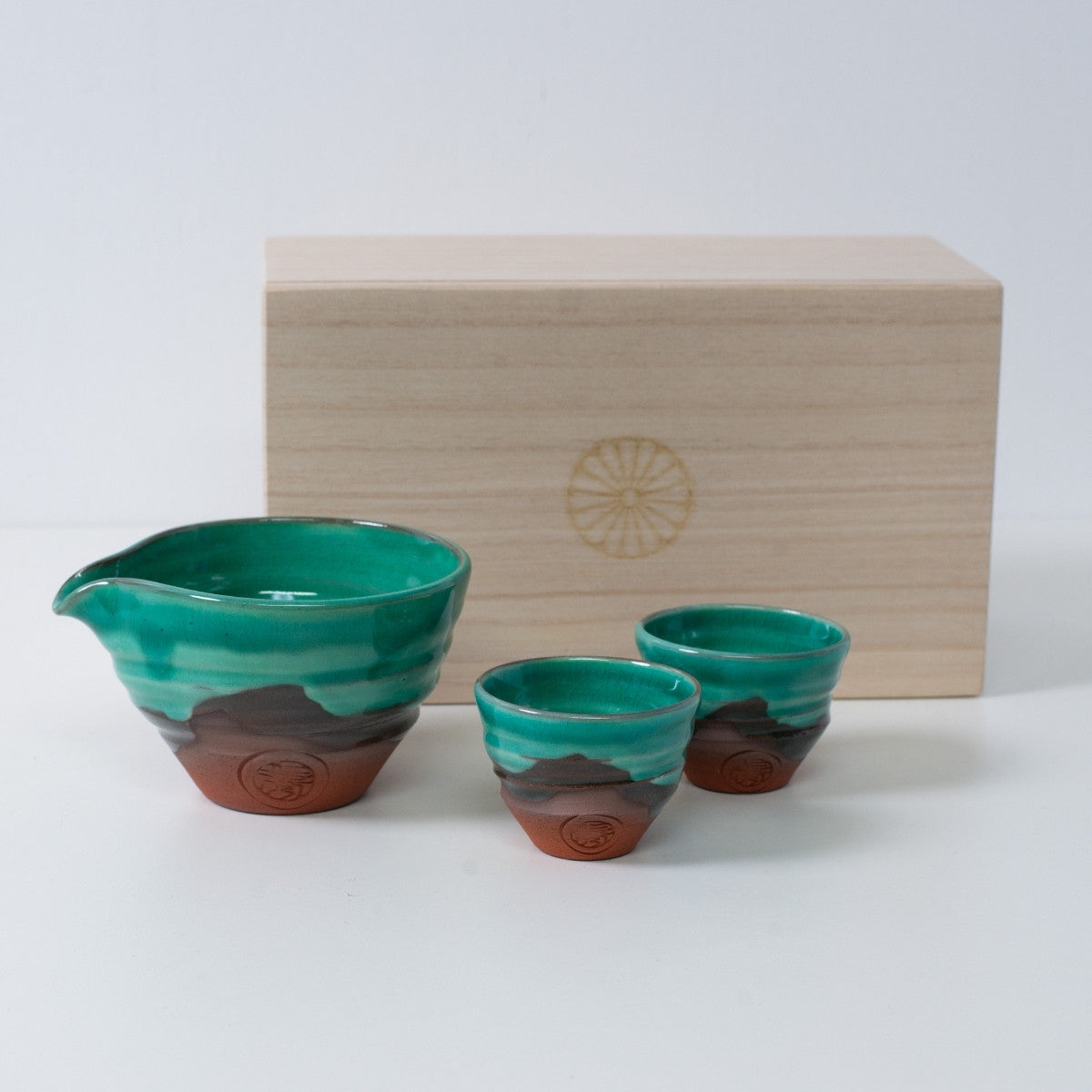 Emerald green and orange Japanese sake set "Emerald" pottery with a sake carafe and two cups, next to a wooden box with a chrysanthemum crest.