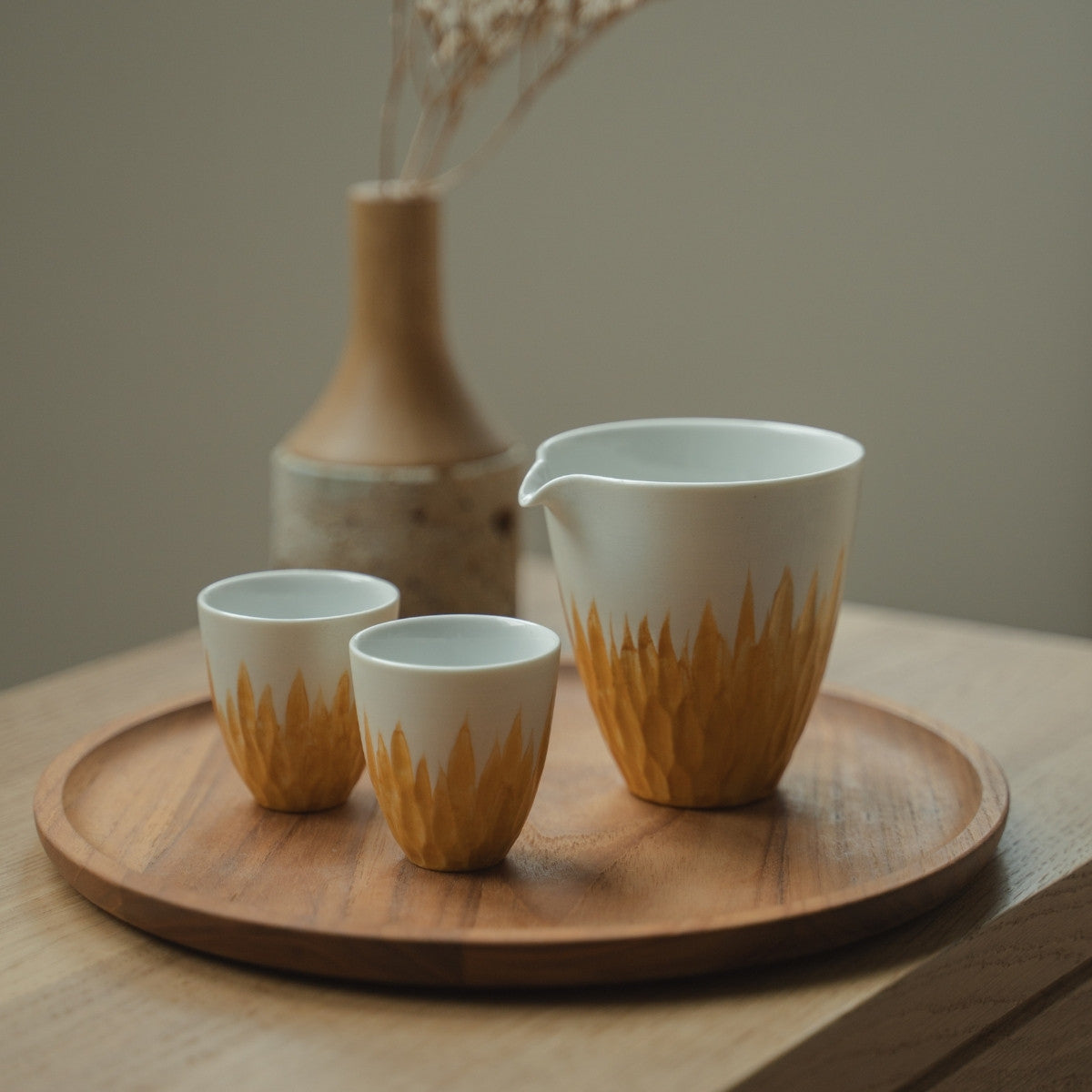 Hvid og guld japansk sake-karaffel og sake-kopper på en træbakke, der byder gæster velkommen til et lyst Japandi-spisestue.