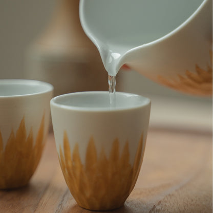 Hældning af klar sake fra en hvid og guldfarvet japansk sakekaraffel ned i en kop, hvilket løfter en festlig middag for gæster.