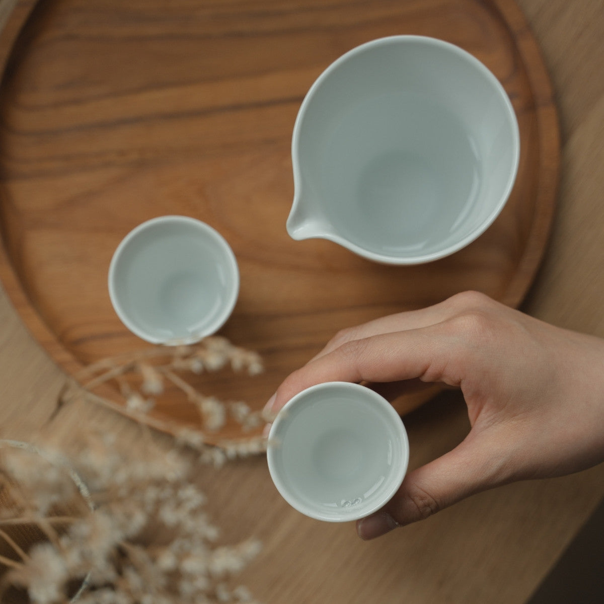 Hånd holder en hvid arita porcelæn sake kop over et bakke, forbereder sake-elskere til en mindful og elegant aften.