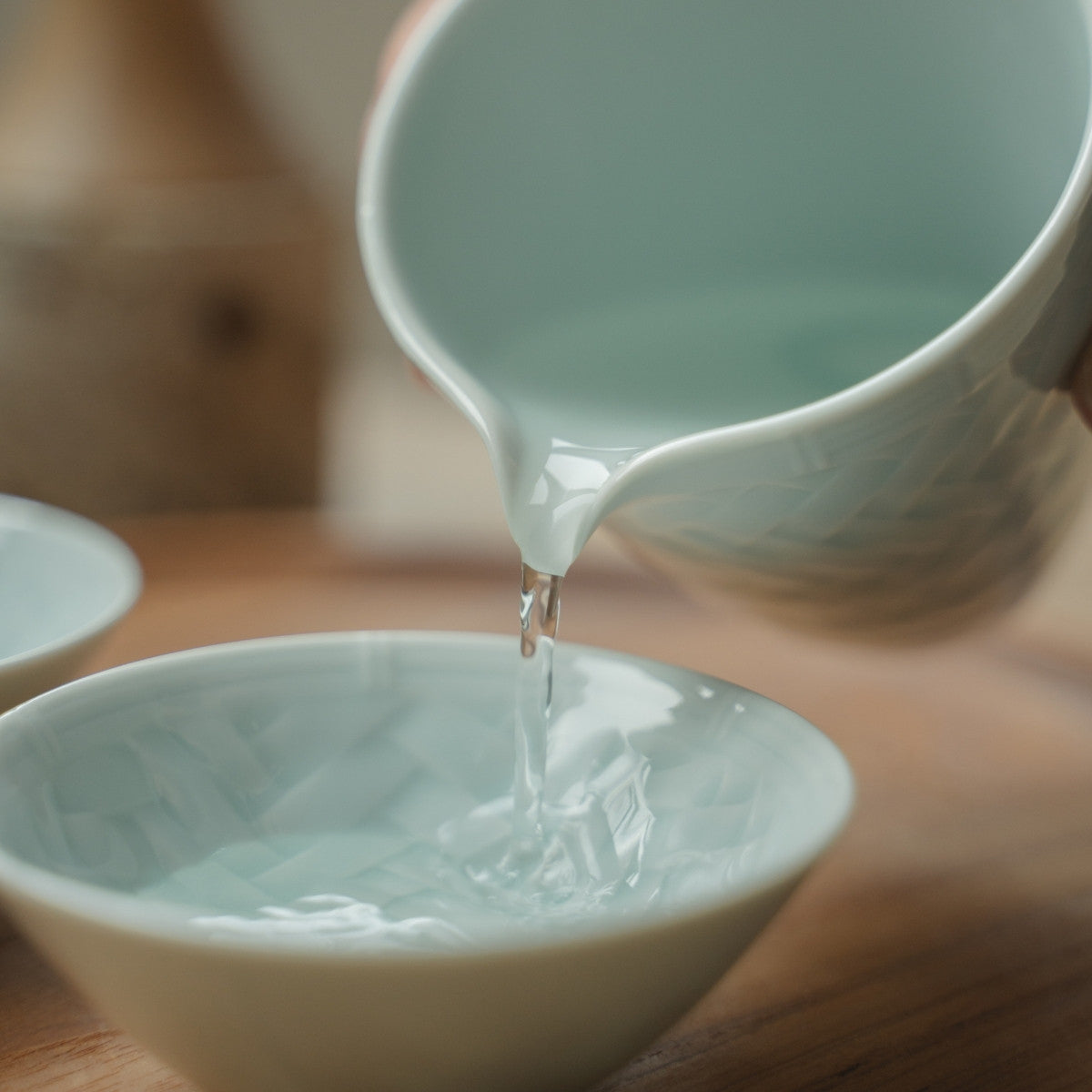 Verser à la main depuis une carafe à saké japonaise bleu glacier dans une tasse à saké texturée, rehaussant un dîner spécial.