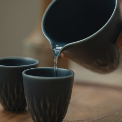 Matte blue Japanese sake pitcher pouring clear sake into a cup, elevating a special dinner gathering for guests.