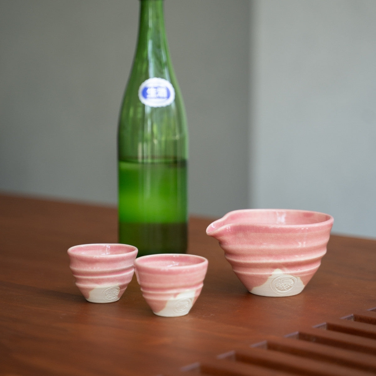 Pink Japanese Kyo-yaki pottery sake set (katakuchi carafe, two cups) on a Japandi style wood table, ready for a special evening dinner.