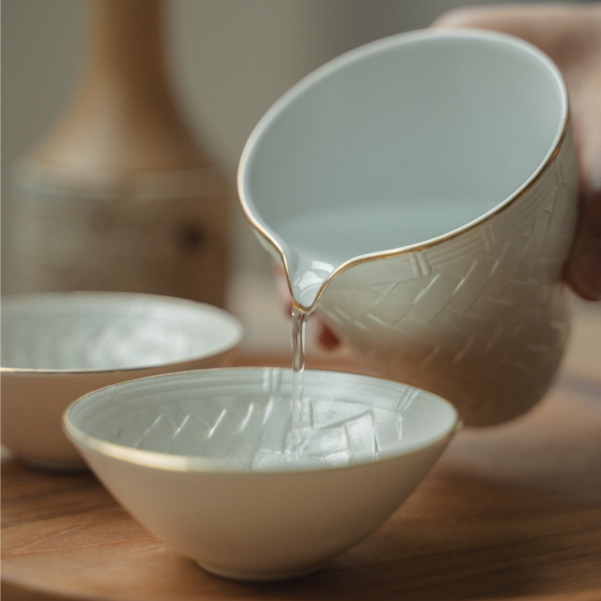 Handgeschöpft aus einer weißen japanischen Sake-Kanne in eine zarte Guinomi-Tasse auf einem Holztablett, was ein besonderes Abendessen aufwertet.