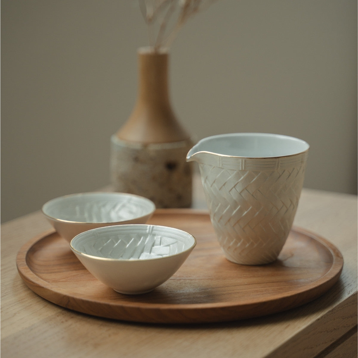 Weiße japanische Arita-Porzellan-Sake-Karaffe und Sake-Becher aus Japan auf einem Holztablett, arrangiert für ein achtsames Esserlebnis mit Gästen.