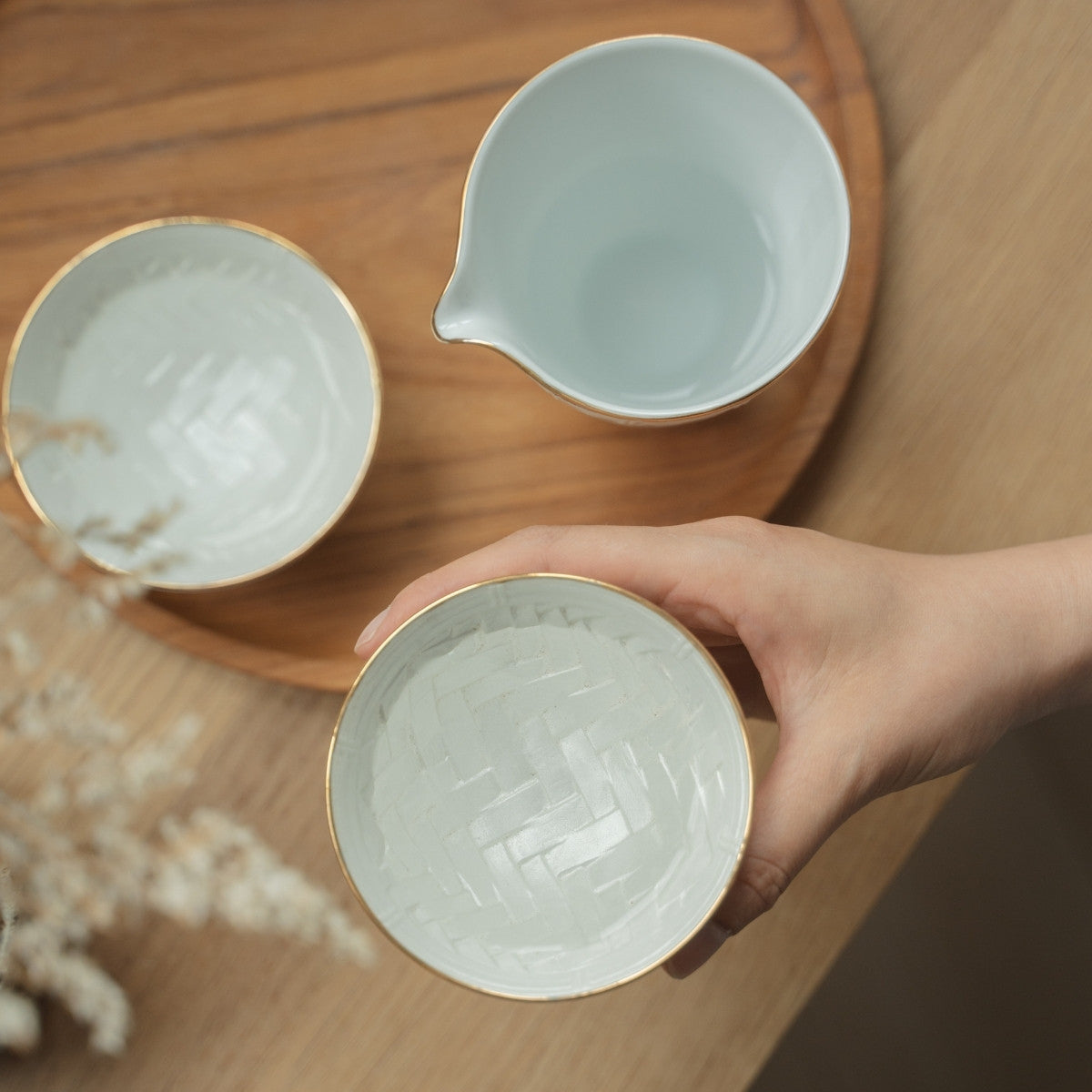 Hand hält eine strukturierte weiße japanische Arita-Porzellan-Sake-Tasse über einem Holzteller, die Sake-Liebhaber zu einem ruhigen Abend einlädt.