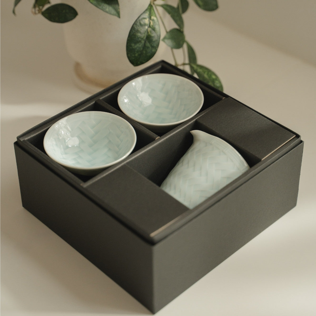 Ensemble de saké en porcelaine arita blanche du Japon dans une élégante boîte cadeau noire sur une table moderne, prêt à offrir aux amateurs de saké.