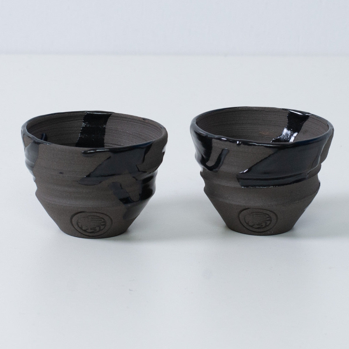 To japanske sakekopper ochoko "Sumi Black" keramik fra Japan, med et indgraveret håndværkersegl på forsiden af hver kop.