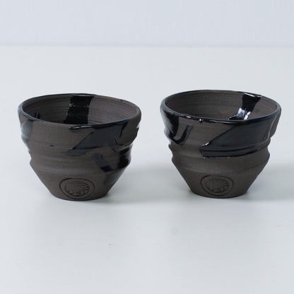 To japanske sakekopper ochoko "Sumi Black" keramik fra Japan, med et indgraveret håndværkersegl på forsiden af hver kop.