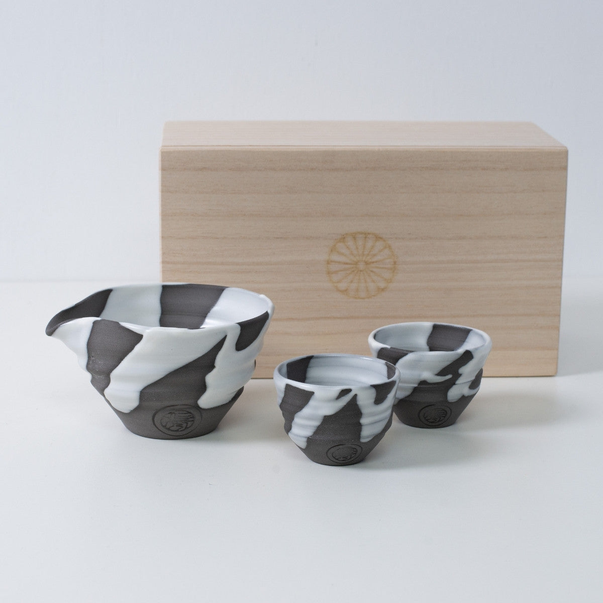 White and gray Japanese sake set "White Flow" pottery with a sake carafe and two cups, next to a wooden box with a chrysanthemum crest.