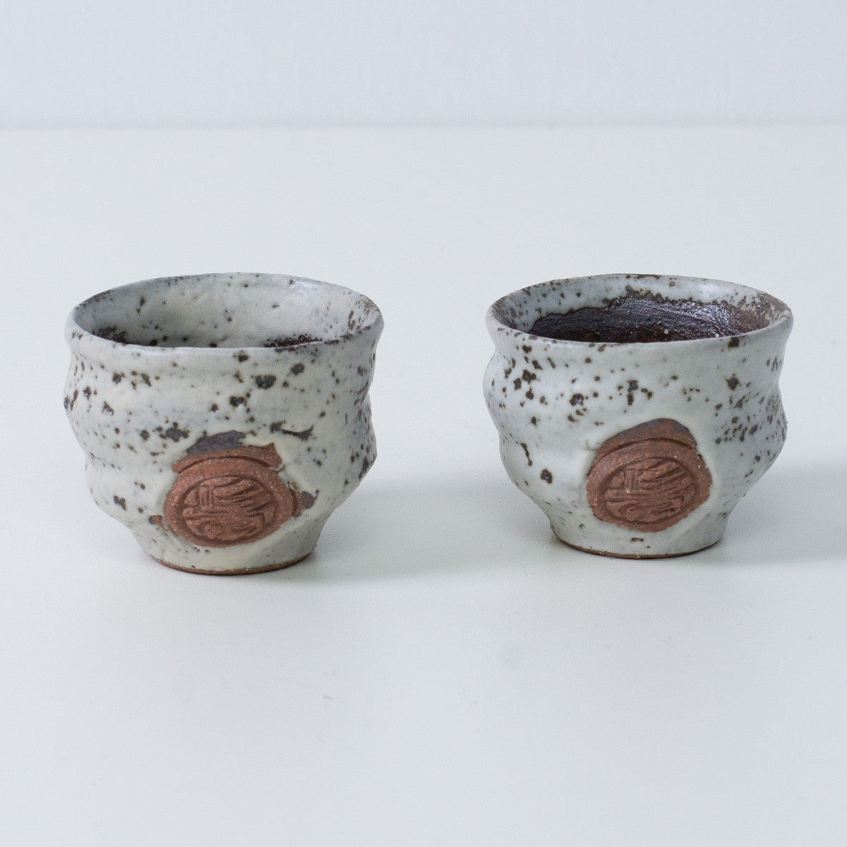 Two brown and white Japanese sake cups ochoko "Zui" pottery from Japan, featuring an engraved brown artisan seal on the front.