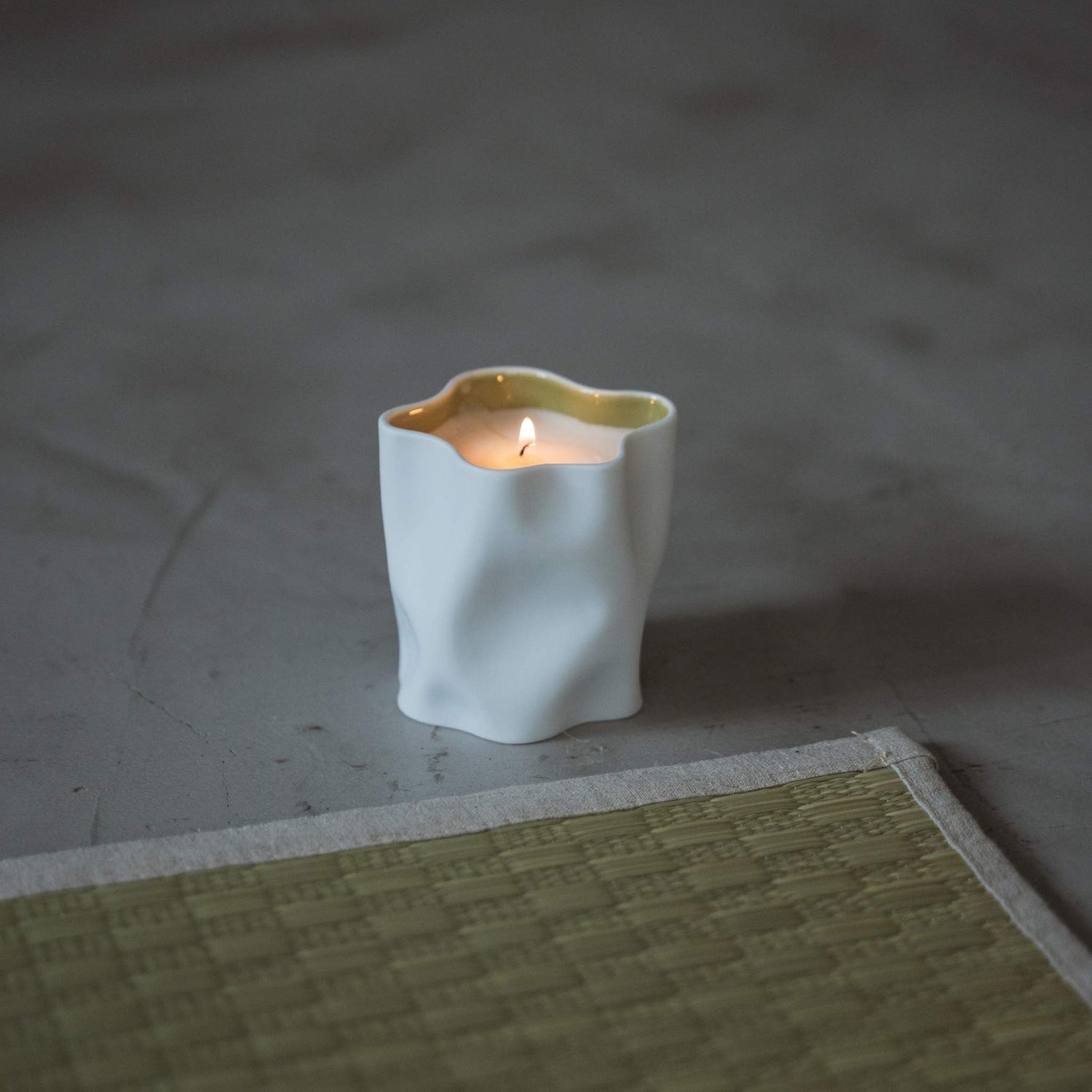 Japanische Yuzu-Duftkerze in einem weißen Porzellangefäß, die mit einer sanften Flamme neben einer Tatami-Matte brennt.