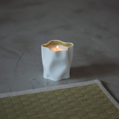 Japanische Yuzu-Duftkerze in einem weißen Porzellangefäß, die mit einer sanften Flamme neben einer Tatami-Matte brennt.