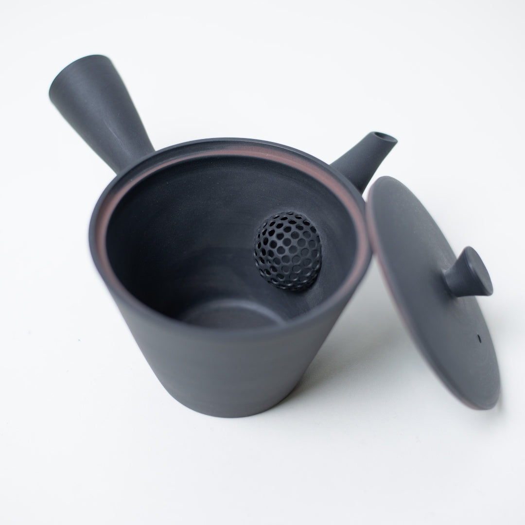 Åben japansk tekande, der kigger ind på den keramiske si og låget på den sorte kyusu sencha-kande