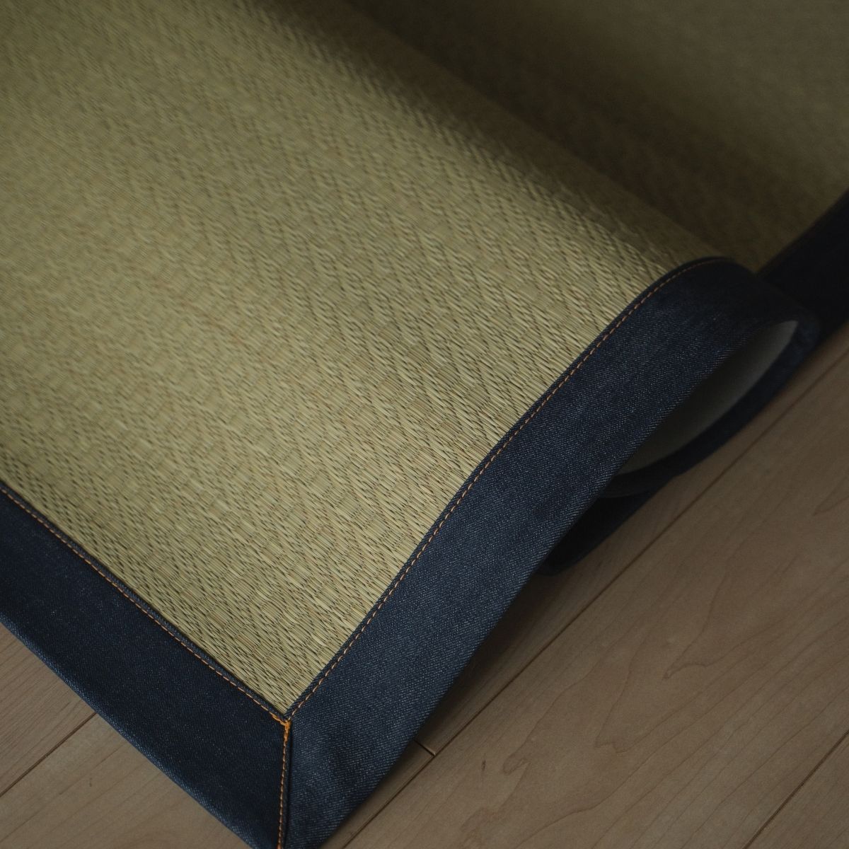 Japanese denim rush tatami area rug folded on a wood floor, adding a stylish indigo accent to modern Japanese decor.