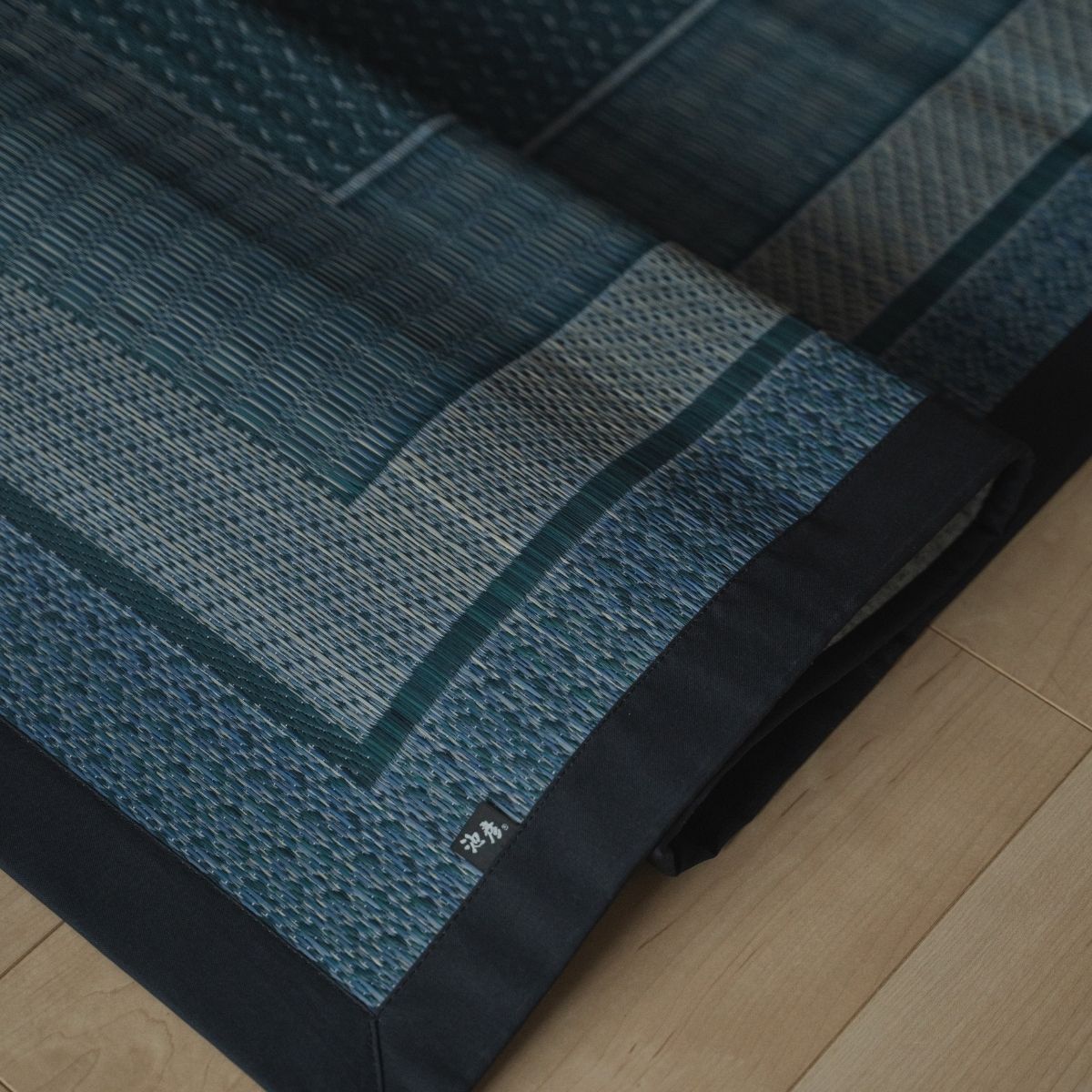 Japanse indigo marineblauwe rush tatami vloerkleed opgevouwen op een houten vloer, met een geometrisch patroon voor een moderne Japanse inrichting.