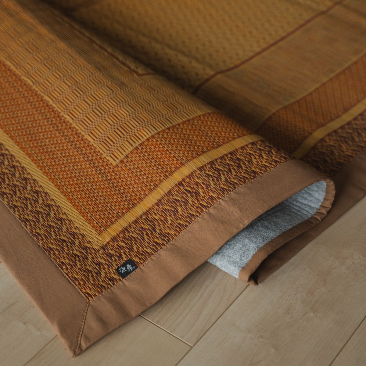 Japanse natuurlijke beige rieten tatami vloerkleed, opgevouwen op een houten vloer, dient als stijlvolle tatami mat voor Japandi kamers.