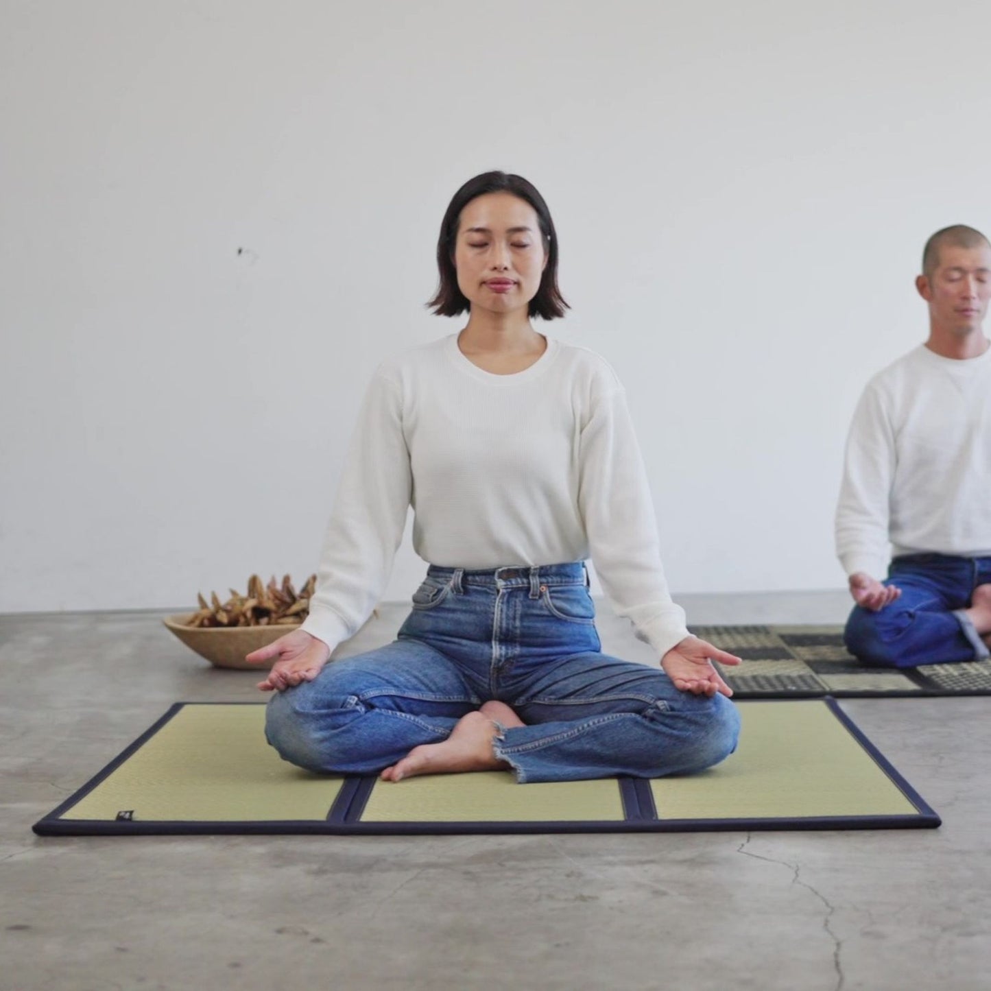 "Vrouw mediterend op een gladde, ongeverfde tatamimat, mindfulness beoefenend in een rustige en minimale ruimte."