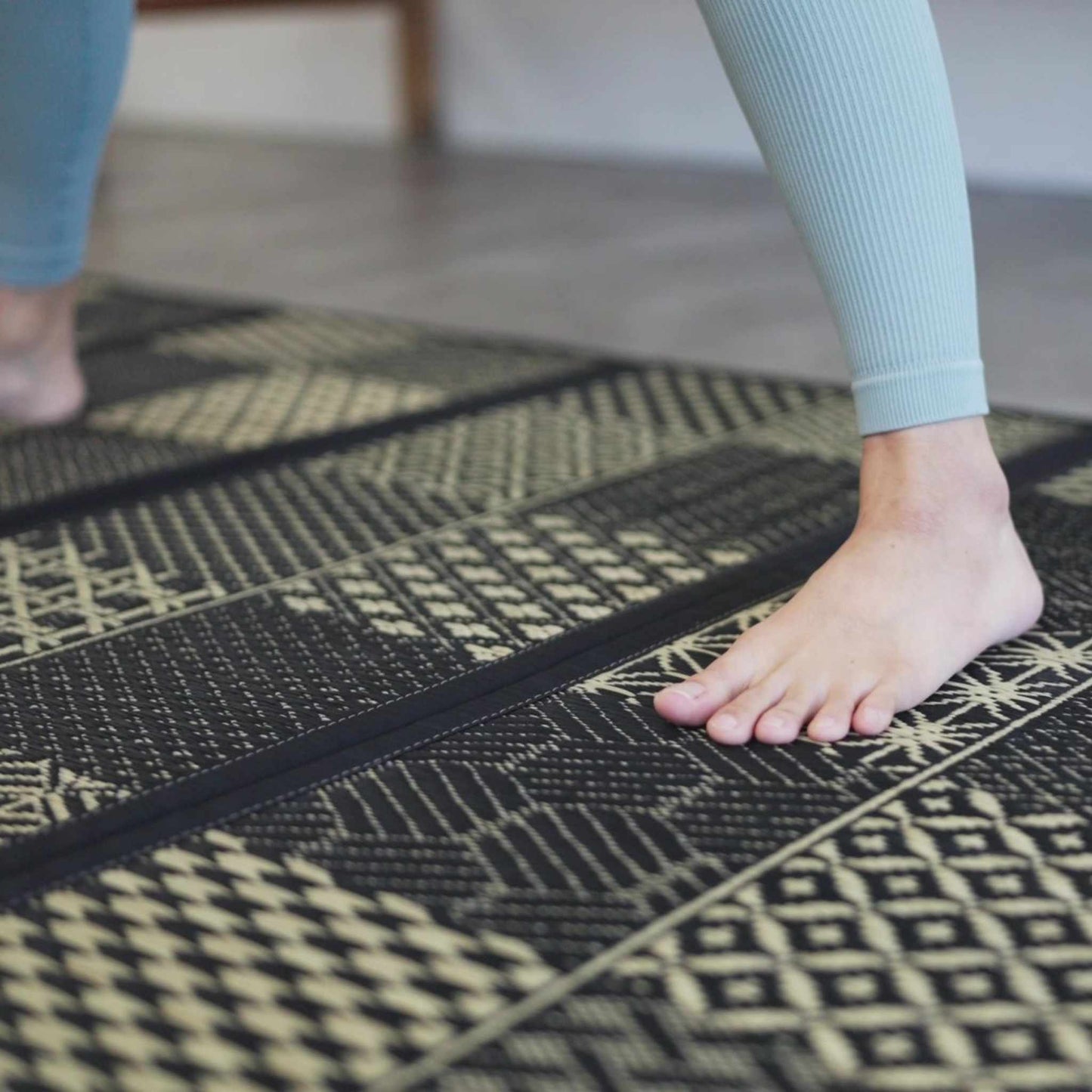 Close up of feet on a black patterned tatami mat showing the woven texture ideal for yoga and barefoot living.