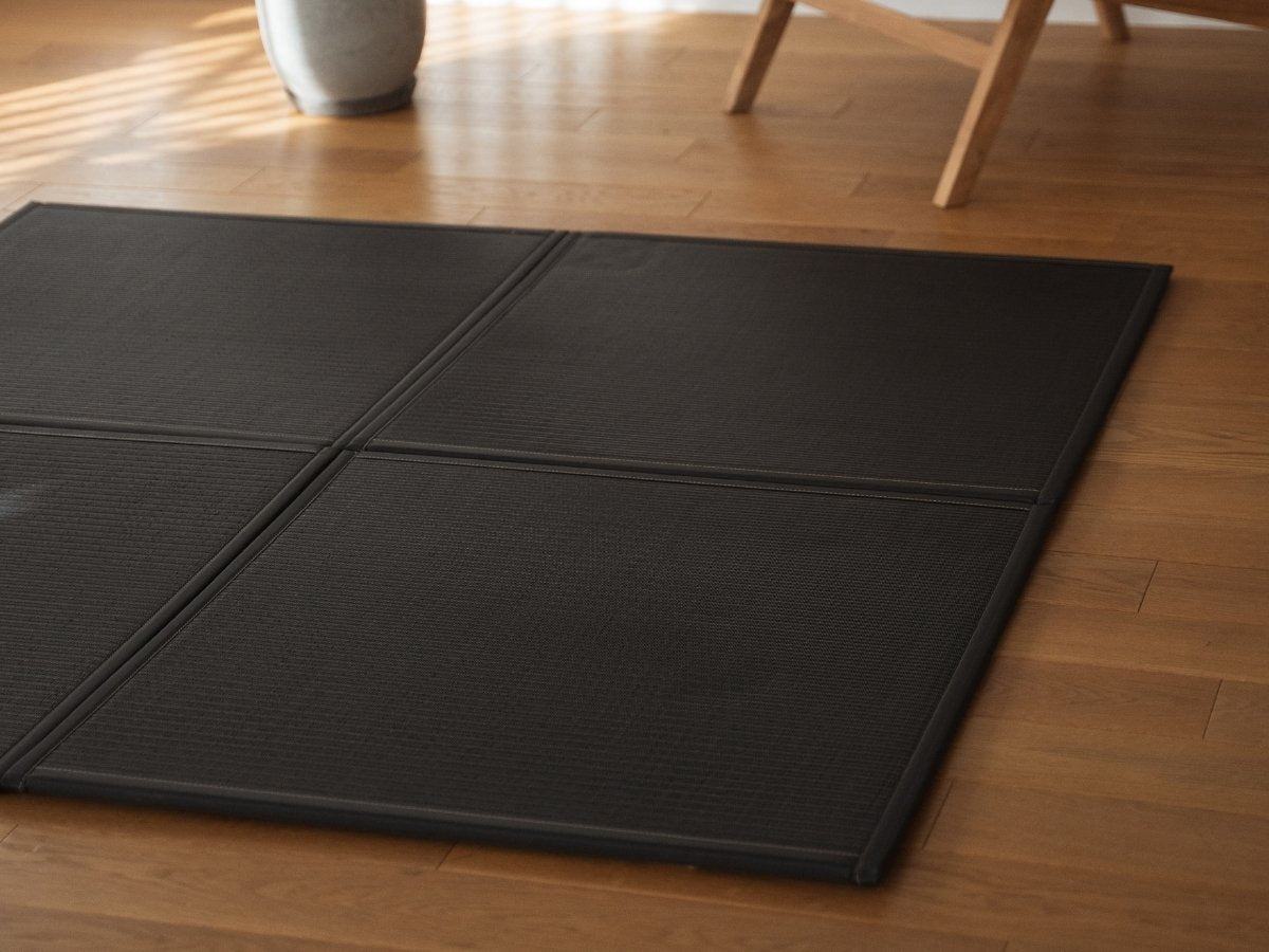 Vier schwarze Tatami-Matten in Einheitengröße, angeordnet auf dem Boden eines japanisch-skandinavischen Wohnzimmers, dienen als moderner und langlebiger Zen-Deko-Teppich.